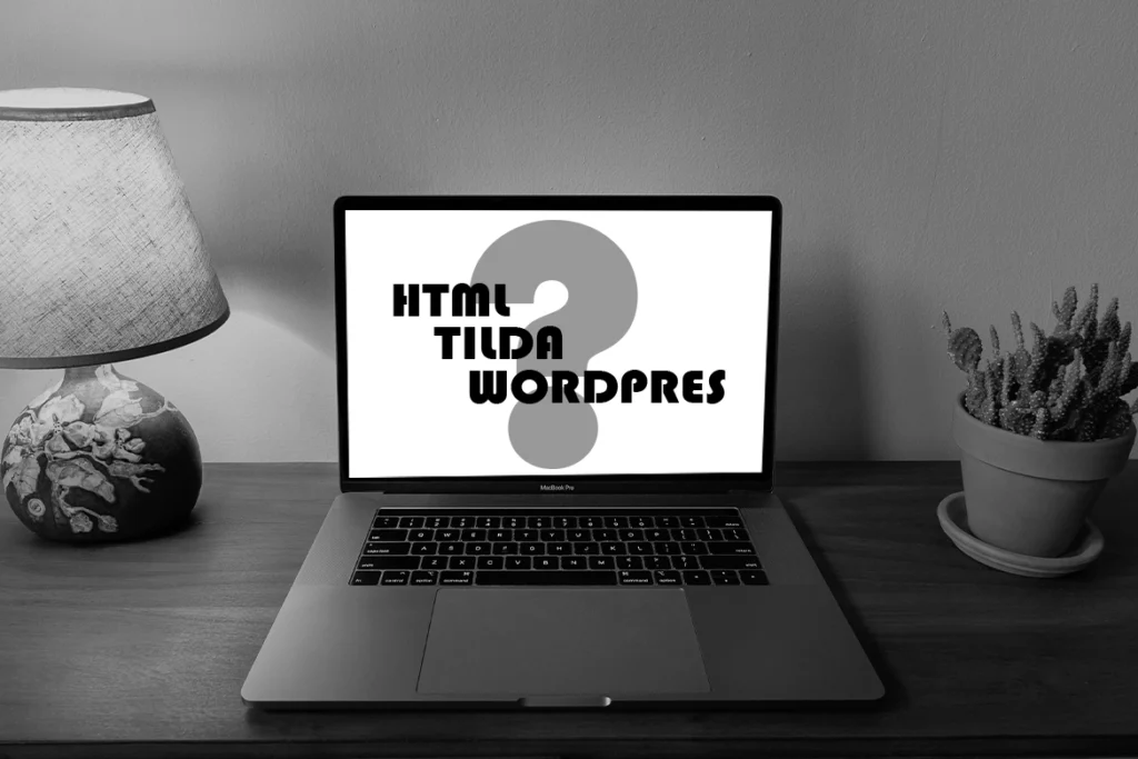 Foto in bianco e nero di una scrivania con lampada e pianta, al centro un laptop acceso che mostra sullo schermo un grande punto interrogativo e le scritte “HTML”, “Tilda”, “WordPress”.